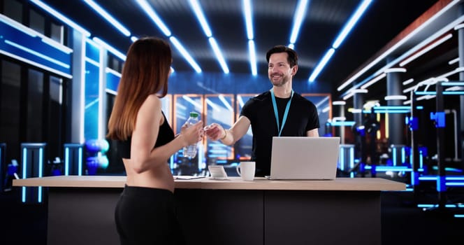 Female athlete paying for gym membership with smartphone to receptionist.