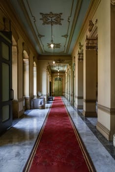 Bangkok, Thailand - Mar 02, 2025 - Perspective hallway leading with ceiling hanging lamp and pillars leading into entrance green ancient door inside The main Bang Khun Phrom Palace or Bank of Thailand Museum. use it as your Wallpaper, Poster and Space for text, Selective focus.