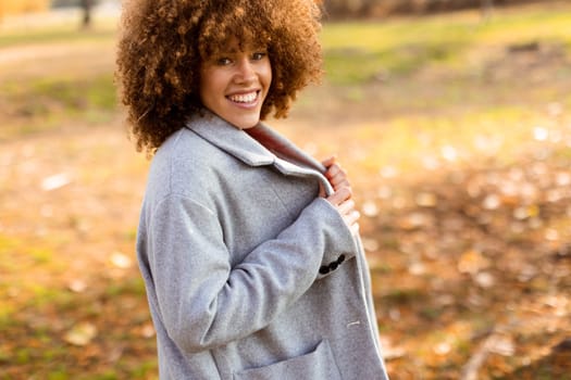 Bright autumn day captivates as a young woman walks through a lovely park, dressed in a cozy gray coat and red sweater, embodying warmth and joy amidst nature's beauty.