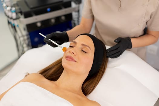 A woman enjoys a luxurious skincare treatment, lying on a treatment bed while a skilled aesthetician gently applies a soothing serum to her face in a serene spa environment.