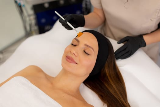A woman enjoys a luxurious skincare treatment, lying on a treatment bed while a skilled aesthetician gently applies a soothing serum to her face in a serene spa environment.