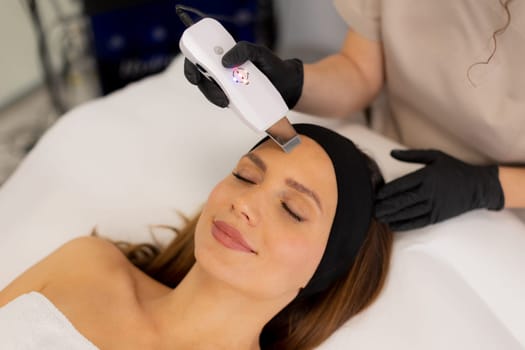 A skilled therapist gently uses an ultrasonic facial massager on a client's forehead, enhancing relaxation and skincare in a tranquil spa environment during a rejuvenating session.