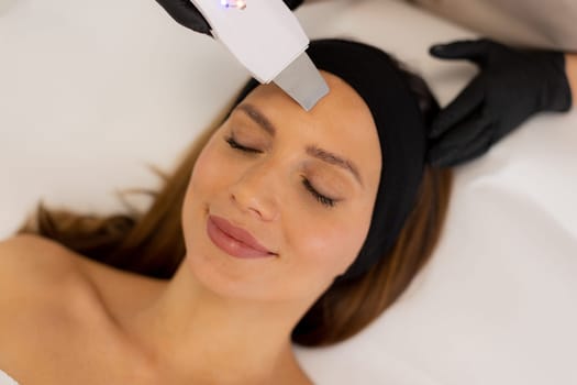 A skilled therapist gently uses an ultrasonic facial massager on a client's forehead, enhancing relaxation and skincare in a tranquil spa environment during a rejuvenating session.