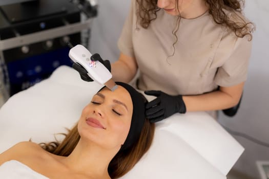 A skilled therapist gently uses an ultrasonic facial massager on a client's forehead, enhancing relaxation and skincare in a tranquil spa environment during a rejuvenating session.