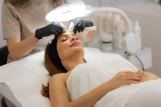 A woman enjoys a rejuvenating facial treatment at a tranquil spa. A skilled aesthetician gently wipes her forehead, enhancing her pampering experience.