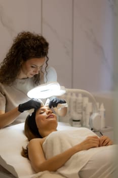 A woman enjoys a rejuvenating facial treatment at a tranquil spa. A skilled aesthetician gently wipes her forehead, enhancing her pampering experience.