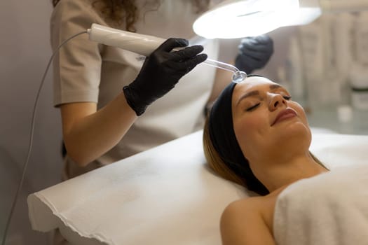 A therapist administers a high frequency therapy treatment, utilizing a glass electrode over a client's face. The process aims to refresh and revitalize the skin in a tranquil setting.