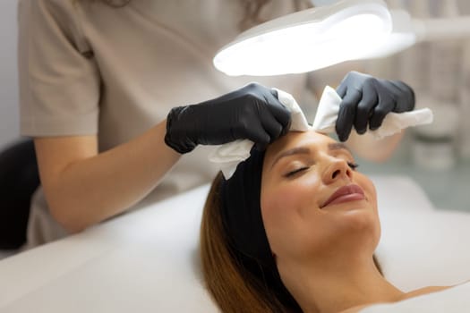 A woman enjoys a rejuvenating facial treatment at a tranquil spa. A skilled aesthetician gently wipes her forehead, enhancing her pampering experience.