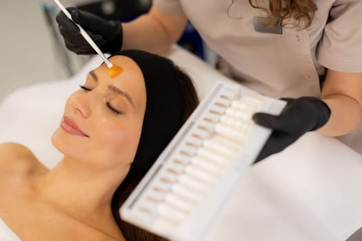 A skilled aesthetician gently applies a vibrant retinol serum to a client's forehead, enhancing her skincare routine in a tranquil spa setting filled with soothing decor.