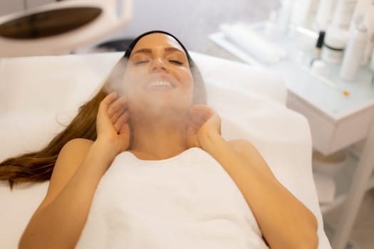 A woman lies back with a content smile while enjoying a steam facial at a spa. The calming atmosphere enhances her rejuvenation, creating a serene and inviting experience.