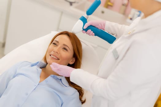 Patient relaxes on a treatment bed as a skilled technician uses a CO2 skin cooling device to enhance comfort during a facial rejuvenation procedure in a contemporary clinic environment.