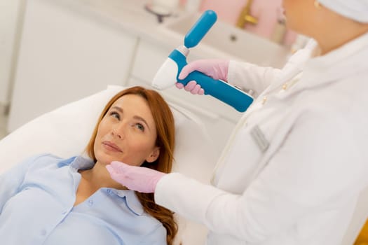 Patient relaxes on a treatment bed as a skilled technician uses a CO2 skin cooling device to enhance comfort during a facial rejuvenation procedure in a contemporary clinic environment.