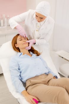 A woman enjoys a refreshing skincare procedure, lying comfortably as a skilled practitioner applies nourishing serum. The atmosphere is calming, promoting relaxation and wellness.
