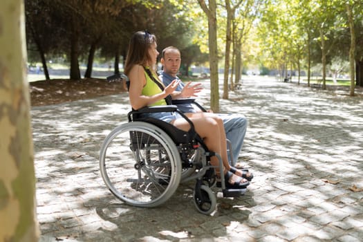 Young woman using wheelchair gesturing while talking with a friend in a park