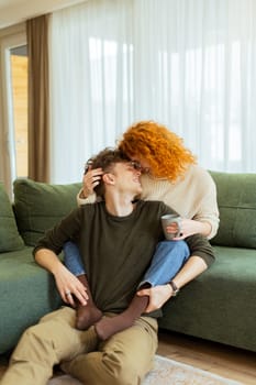 A couple enjoys a relaxing afternoon at home, seated comfortably on a plush sofa, exchanging loving smiles and laughter while sharing a warm beverage together