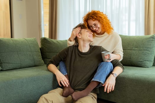 A couple enjoys a relaxing afternoon at home, seated comfortably on a plush sofa, exchanging loving smiles and laughter while sharing a warm beverage together
