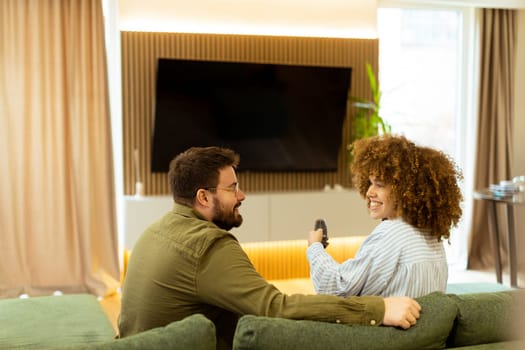 Seated on a comfortable couch, a couple shares a light-hearted moment, laughing and watching their favorite show while surrounded by a warm, inviting atmosphere.