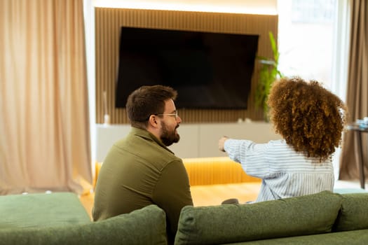 Seated on a comfortable couch, a couple shares a light-hearted moment, laughing and watching their favorite show while surrounded by a warm, inviting atmosphere.