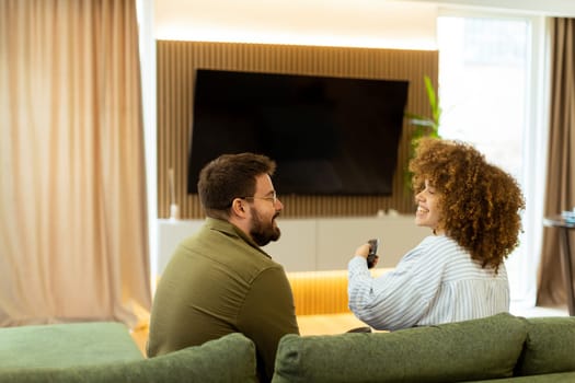 Seated on a comfortable couch, a couple shares a light-hearted moment, laughing and watching their favorite show while surrounded by a warm, inviting atmosphere.