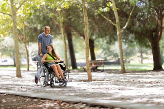 Man assisting a disabled woman in a wheelchair, enjoying a walk through a sunny park