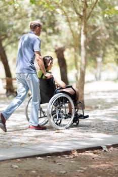 Father assisting his disabled daughter, enjoying a walk in the park on a sunny day
