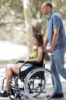Nurse assisting a female patient in a wheelchair on a walk through a sunny park