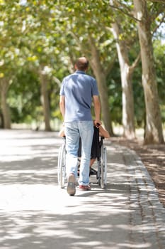 Nurse assisting elderly patient in wheelchair enjoying walk in sunny park