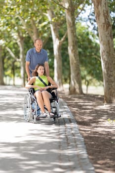 Nurse assisting patient in wheelchair along path in park on sunny day