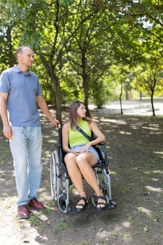 Disabled young woman sitting in wheelchair relaxing with her caregiver in a city park