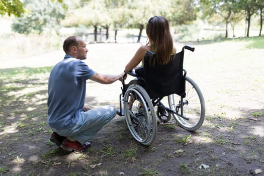 Man crouching next to woman sitting in wheelchair, talking in park