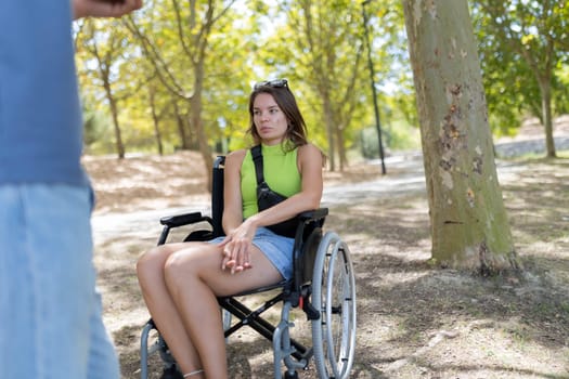 Young woman with physical impairment using wheelchair having a conversation in a park with a friend