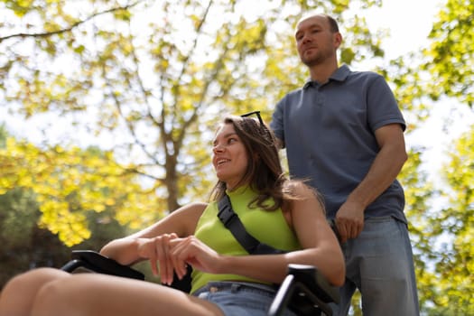 Nurse pushing a smiling disabled woman in a wheelchair through a sunny park during a summer day