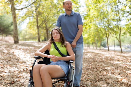 Father standing behind his disabled daughter sitting in wheelchair in park