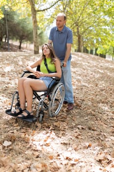 Man assisting a woman in a wheelchair navigating a path in a peaceful park setting