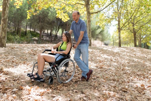 Man assisting a disabled woman in a wheelchair, enjoying a sunny day in the park