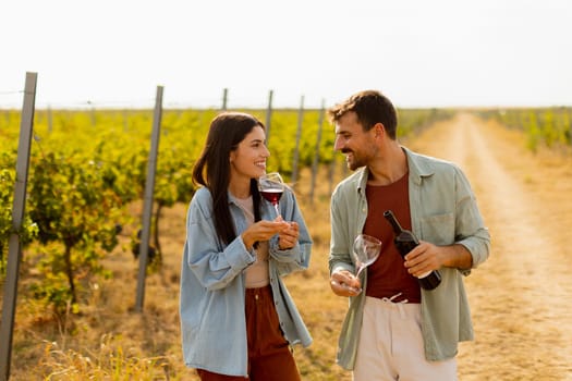 Under the warm glow of the setting sun, a couple shares laughter while sipping wine in a picturesque vineyard, creating cherished memories amid rows of grapevines