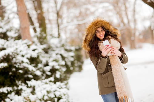 Portrait of smiling young woman with cell phone in winter outdoors