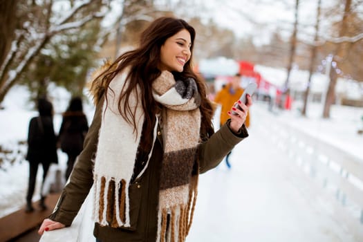 Portrait of smiling young woman with cell phone in winter outdoors
