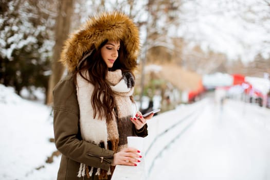 Portrait of young woman in a snow park drinks tea