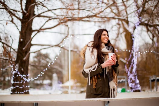 Portrait of young woman in a snow park drinks tea at Christmas market