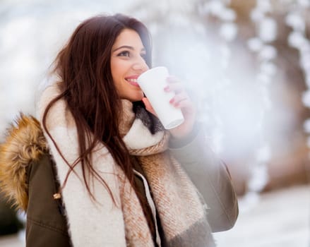Portrait of young woman in a snow park drinks tea at Christmas market