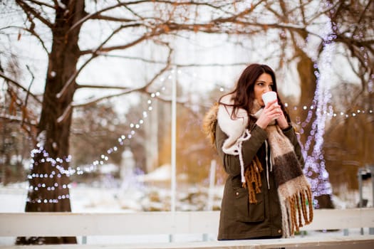 Portrait of young woman in a snow park drinks tea at Christmas market