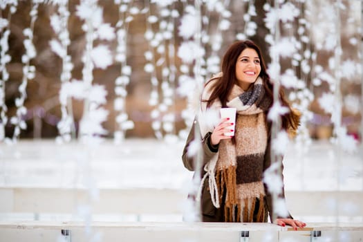 Portrait of young woman in a snow park drinks tea at Christmas market