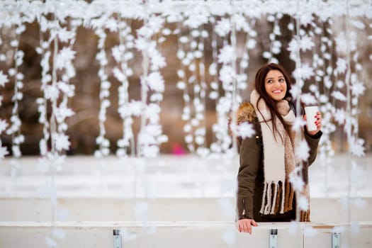 Portrait of young woman in a snow park drinks tea