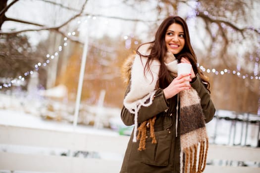 Portrait of young woman in a snow park drinks tea at Christmas market
