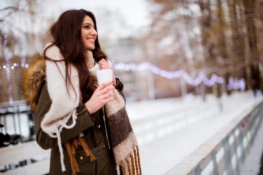 Portrait of young woman in a snow park drinks tea