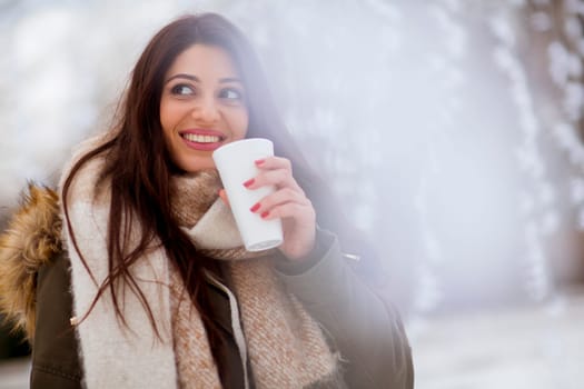 Portrait of young woman in a snow park drinks tea at Christmas market