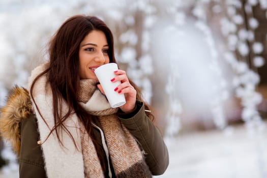 Portrait of young woman in a snow park drinks tea at Christmas market