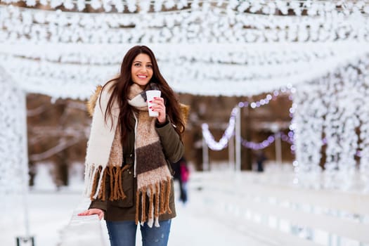 Portrait of young woman in a snow park drinks tea at Christmas market