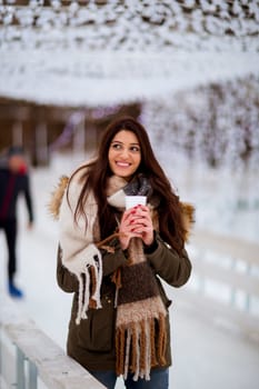 Portrait of young woman in a snow park drinks tea at Christmas market